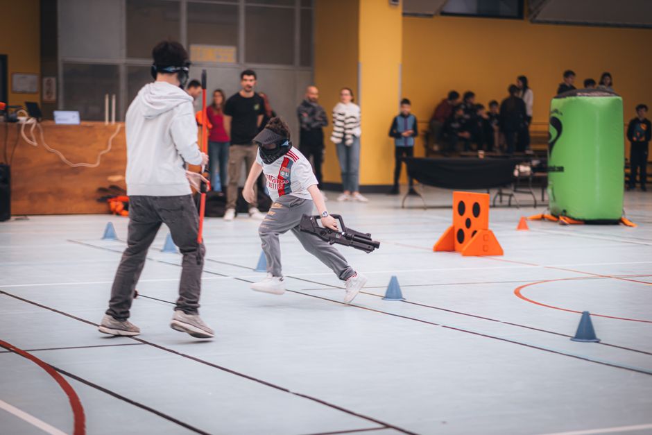 Jovens participando de uma atividade de lazer ou jogos de equipe em um espaço indoor, com público observando ao fundo.