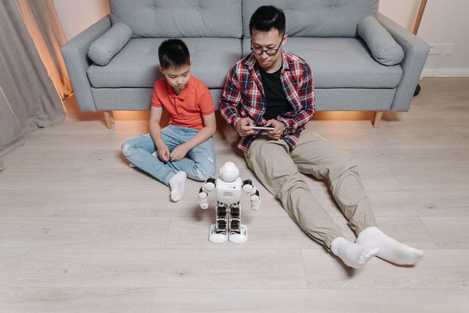 Pai e filho interagindo com um robô em um ambiente doméstico, ilustrando tecnologia e educação em casa.