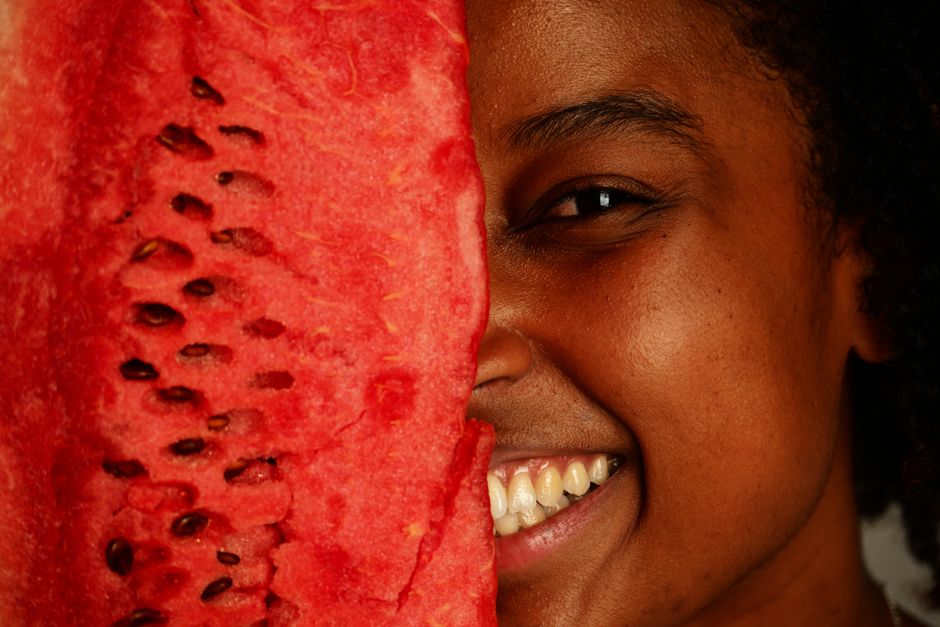 Pessoa sorridente segurando uma fatia de melancia, representando saúde, bem-estar e alimentação saudável.