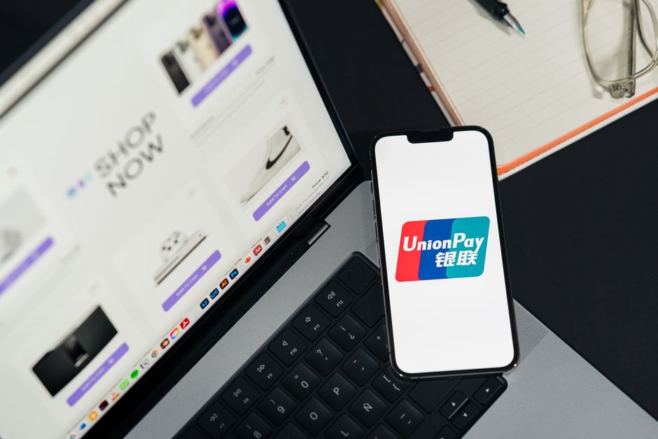 Imagem de uma configuração de trabalho digital com foco em pagamento online, apresentando um laptop, um smartphone exibindo o logo do UnionPay, e acessórios de escritório.