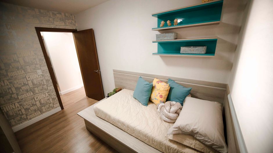 Imagem de um quarto decorado com uma cama simples, almofadas coloridas e prateleiras decorativas na parede, ideal para ilustrar dicas de decoração ou organização de ambientes pequenos.