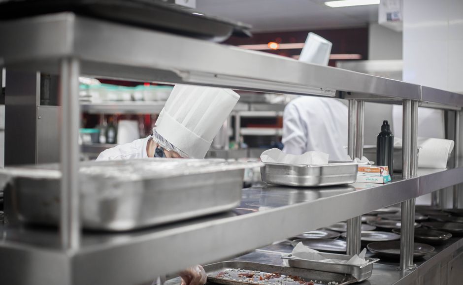 Imagem de uma cozinha profissional com chefs preparando alimentos de forma organizada e higienizada, destacando a rotina em ambiente gastronômico.