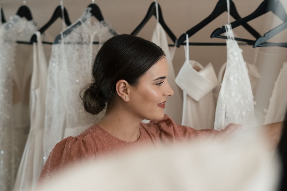 Mulher cuidando de vestidos de noiva enquanto escolhe roupas para um evento especial, em uma loja de noivas.