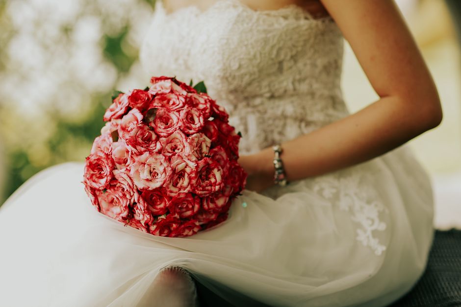 Mulher vestida de casamento segurando um buquê de flores em um ambiente ao ar livre, simbolizando celebração e união.