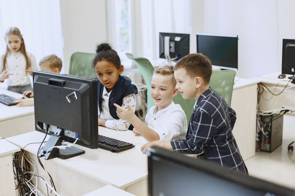 Crianças aprendendo e interagindo com computadores em sala de aula moderna, promovendo educação digital.