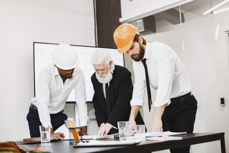 Equipe de engenheiros e um profissional mais experiente analisando projetos em uma reunião de planejamento técnico.