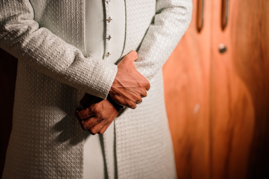 Imagem de uma pessoa vestida com traje formal, com as mãos cruzadas à frente, em ambiente de negócios ou evento oficial.