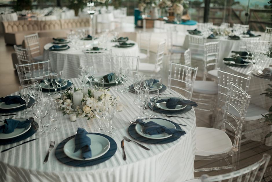 Cenário de evento ou jantar formal em um espaço elegante com mesas decoradas e talheres cuidadosamente arranjados, pronto para recepção de convidados.