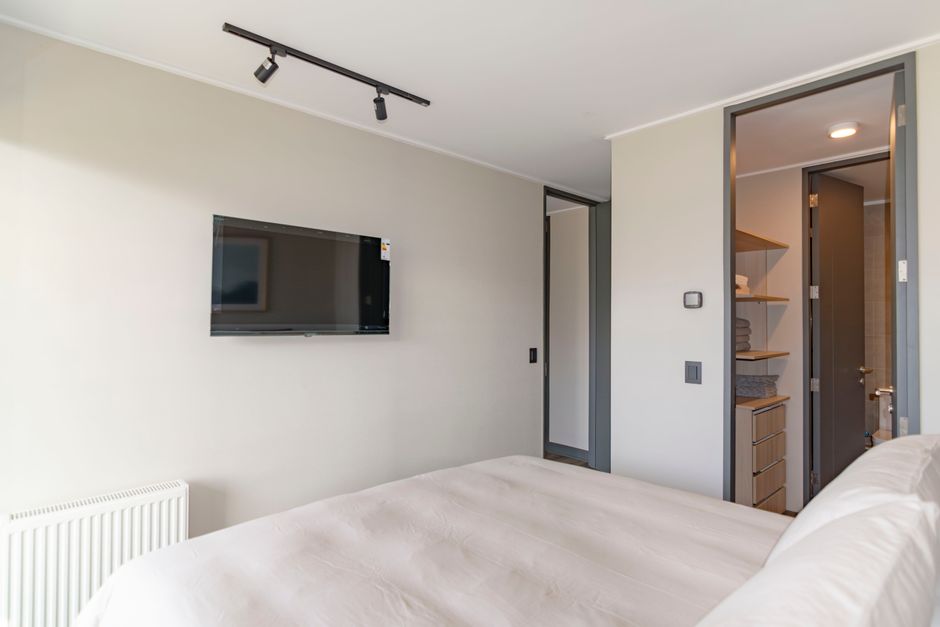 Imagem de um quarto moderno com televisão de tela plana e área de closet, refletindo um ambiente residencial bem decorado.