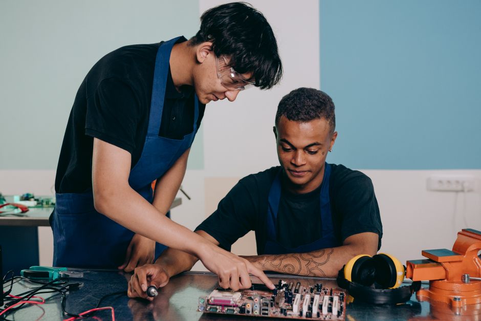 Dois jovens engenheiros trabalham juntos em uma oficina de tecnologia, focados na montagem de um circuito eletrônico.