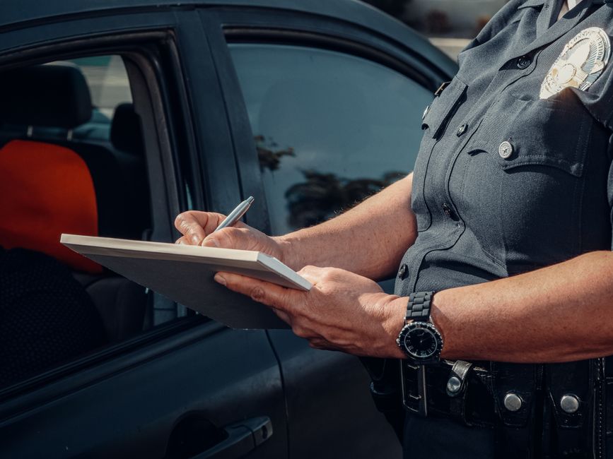 Policial fazendo anotações ao lado de um carro de patrulha em uma operação de fiscalização de trânsito.
