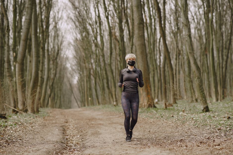 Mulher praticando corrida ao ar livre em uma trilha na floresta, promovendo bem-estar e atividade física.