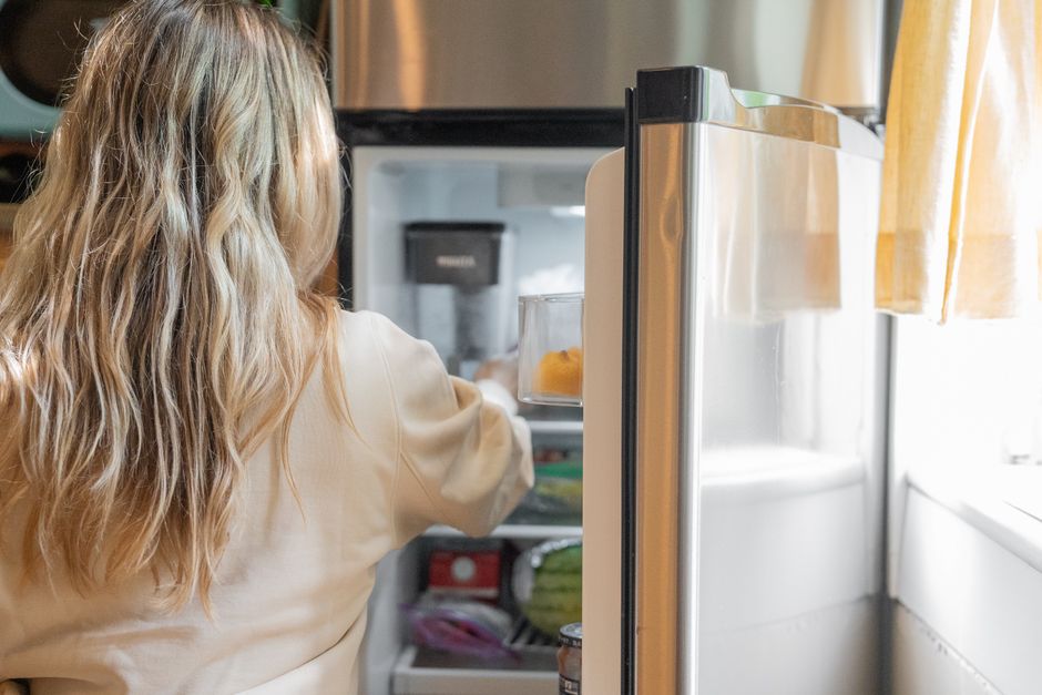 Mulher abrindo a geladeira na cozinha, capturando um momento cotidiano e de autonomia residencial.