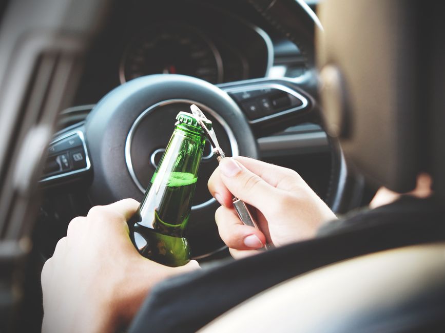 Pessoa abastecendo o carro com uma garrafa de cerveja no posto de combustível, refletindo sobre o consumo de álcool ao dirigir.