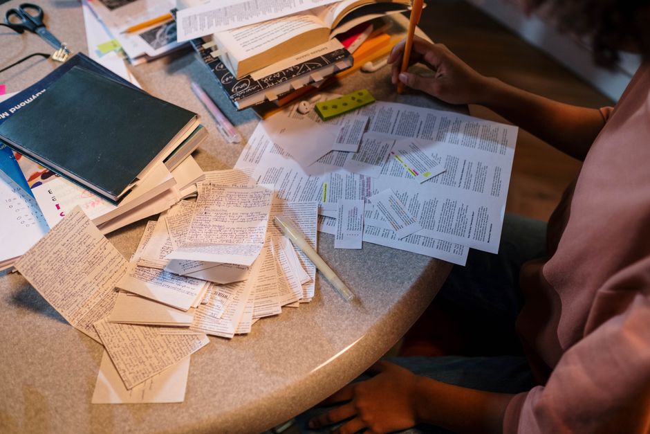 Pessoa estudando e organizando materiais de referência para preparação de um relatório ou trabalho acadêmico.