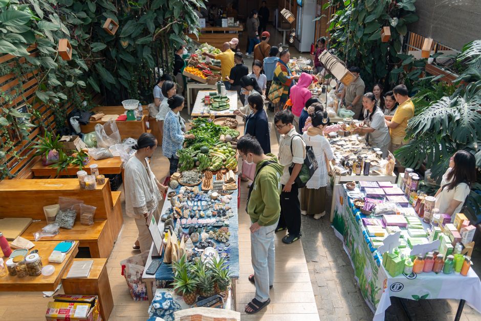 Imagem de um mercado de agricultores indoor com várias bancadas de produtos naturais, alimentos orgânicos e artesanais, atraindo clientes interessados em consumo consciente e sustentável.