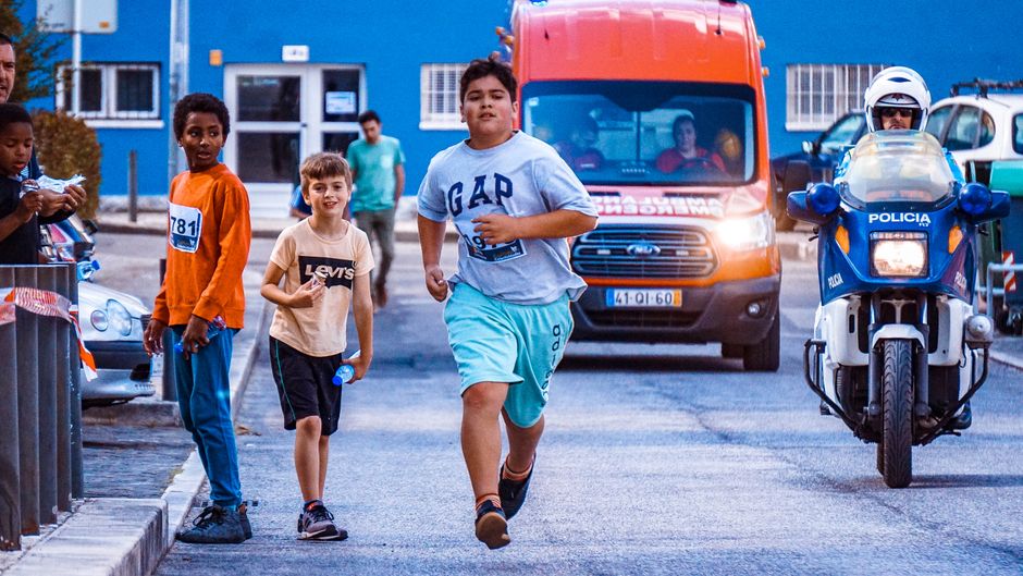 Crianças participando de uma corrida de rua em um evento comunitário na cidade, com apoio de autoridades locais e público presente.