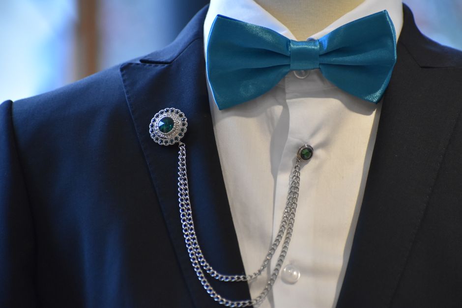 Pessoa vestida formalmente com jaqueta, camisa e gravata borboleta, usando acessórios elegantes, pronto para uma ocasião especial ou evento sofisticado.