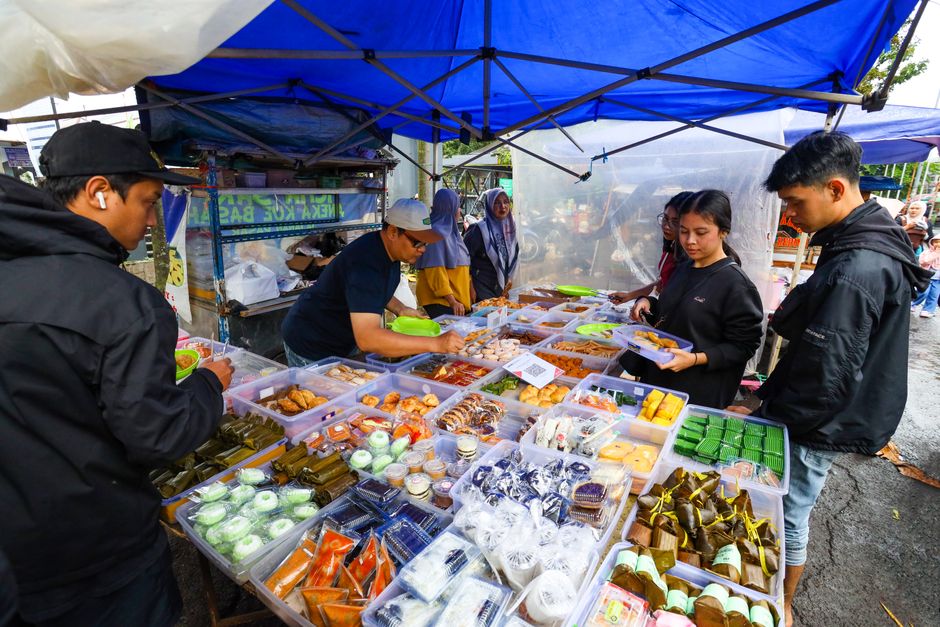 Pessoas fazendo compras em uma feira de alimentos ao ar livre, com estandes de comidas tradicionais e doces.