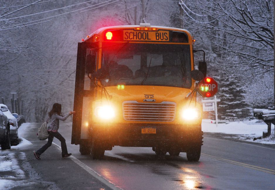 Criança atravessando a rua na frente de um ônibus escolar em uma manhã de inverno com neve na rua.