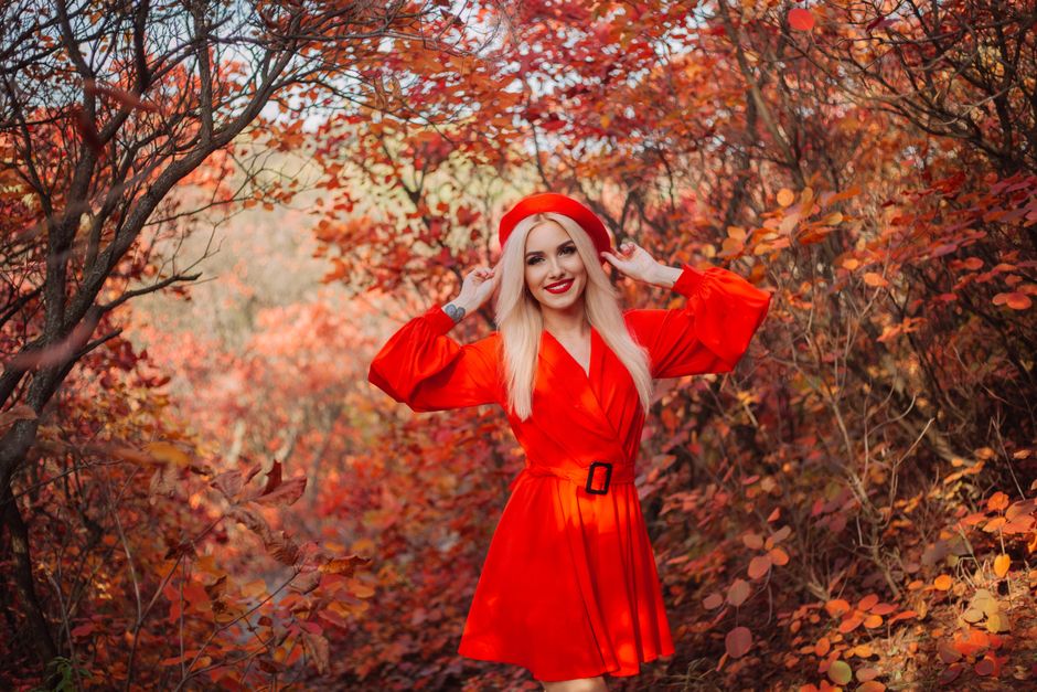 Mulher feliz em um cenário deoutono com árvores de folhas vermelhas, vestida de vermelho, admirando a natureza.