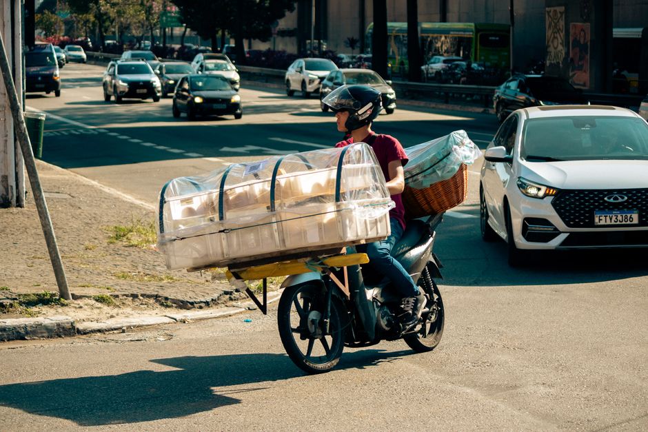 Repartidor de delivery utilizando uma moto para transporte de encomendas em meio ao trânsito urbano, refletindo o tema de logística e entregas rápidas.