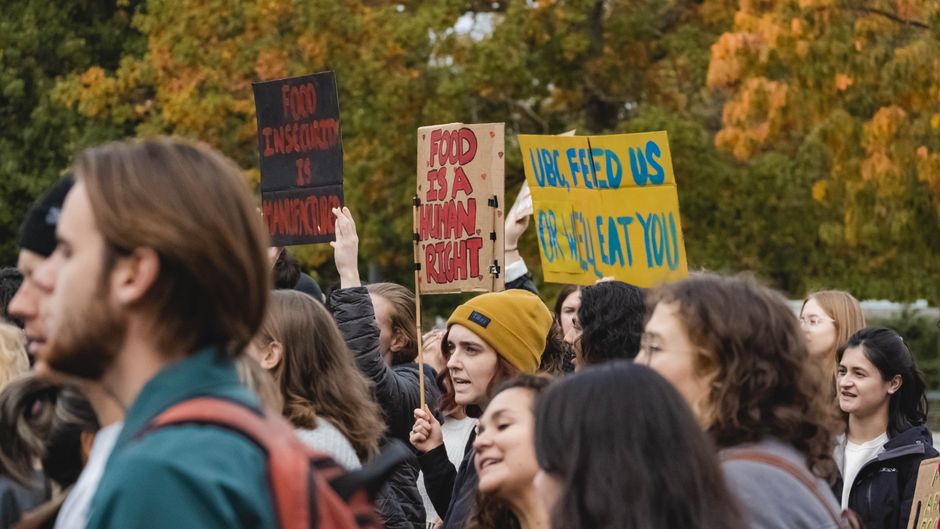 Grupo de pessoas participando de um protesto ou manifestação ao ar livre, com cartazes em mãos, demonstrando engajamento social e ativismo.