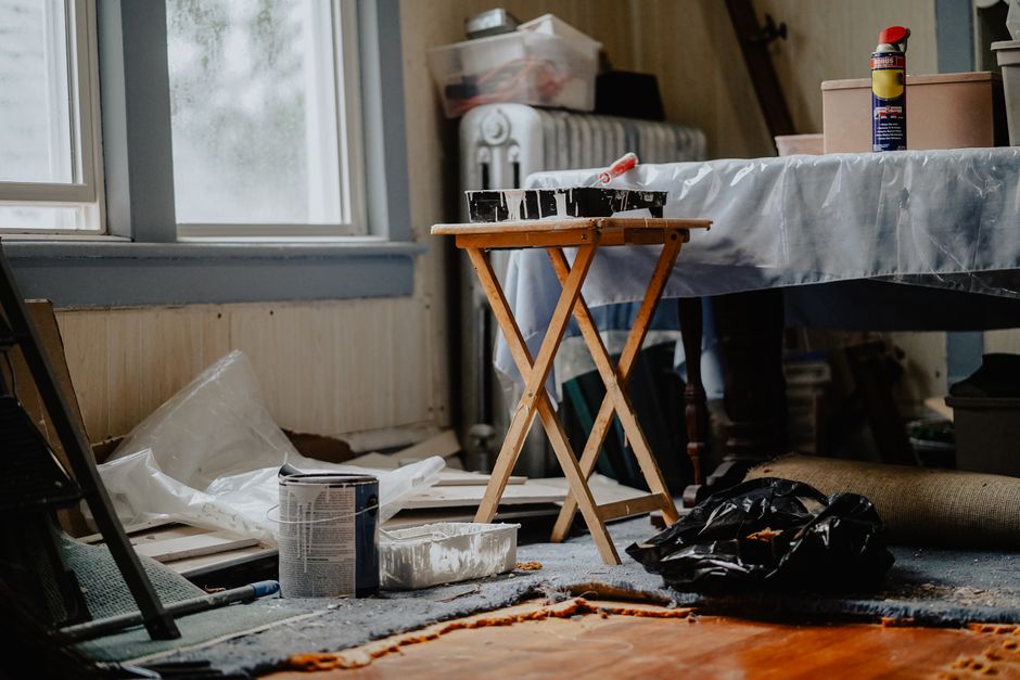Imagem de um espaço de trabalho desorganizado com materiais de pintura e objetos de decoração espalhados, sugerindo um projeto de reforma ou decoração.