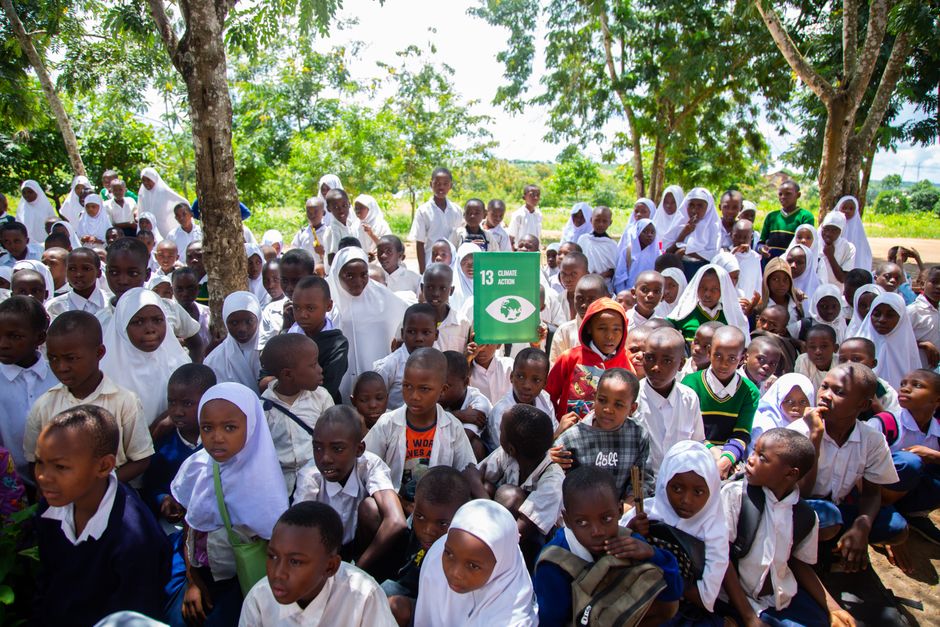 Grande grupo de crianças e adolescentes em ambiente escolar ao ar livre, promovendo conscientização sobre sustentabilidade e educação.