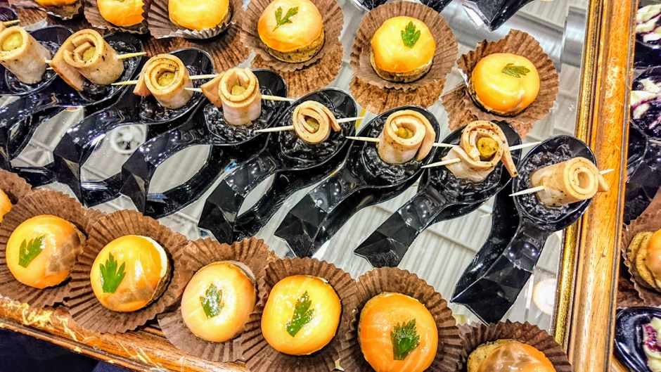 Imagem de docinhos e salgadinhos decorados com folhas verdes em festa ou buffet, com destaque para apresentação sofisticada.