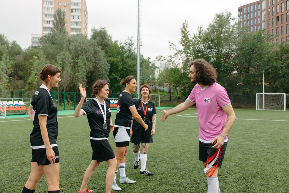 Grupo de mulheres recebendo instruções de um treinador antes de uma partida de futebol em um campo ao ar livre, destacando preparação e trabalho em equipe.