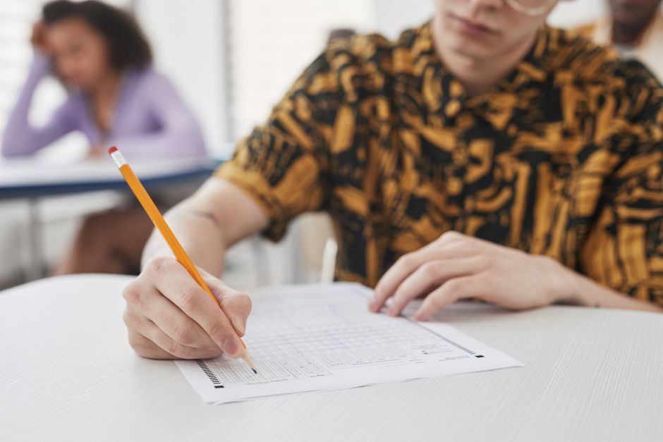 Estudante preenchendo uma ficha ou teste em sala de aula, focado em atividades acadêmicas ou provas.