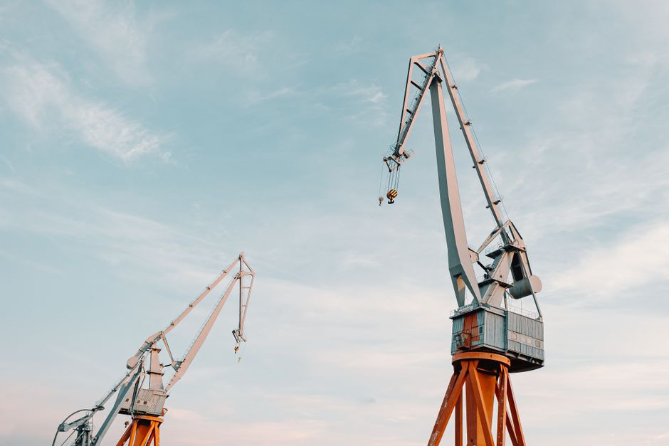 Duas gruas elevando cargas no céu, simbolizando construção e desenvolvimento de grandes projetos.