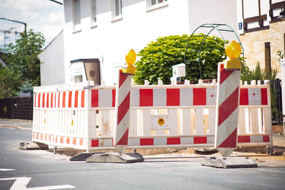 Barreiras de obra bloqueando uma rua residencial com foco em obras e segurança viária.