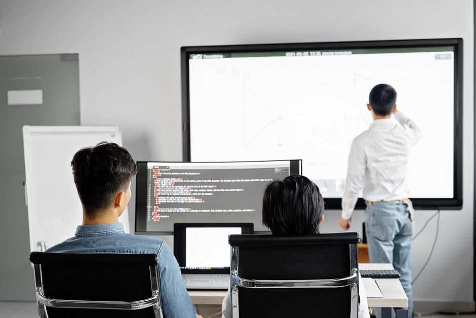 Imagem de uma sala de aula moderna com alunos assistindo uma apresentação, destacando o uso de tecnologia na educação.
