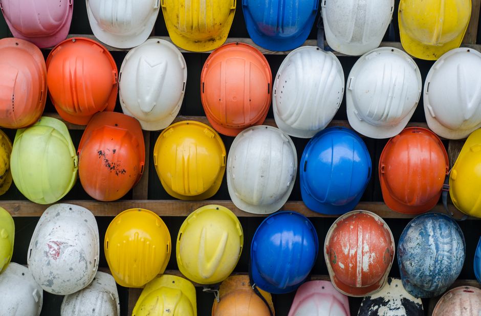 Vários capacetes de proteção coloridos dispostos em uma estrutura de armazenamento, simbolizando segurança e prevenção no ambiente de trabalho.