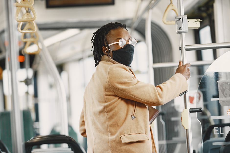 Mulher usando máscara e óculos segurando uma barra dentro de um ônibus urbano, ilustrando o uso de transporte público durante a pandemia.