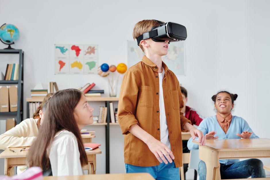 Estudante usando óculos de realidade virtual em sala de aula com colegas atentos ao redor.
