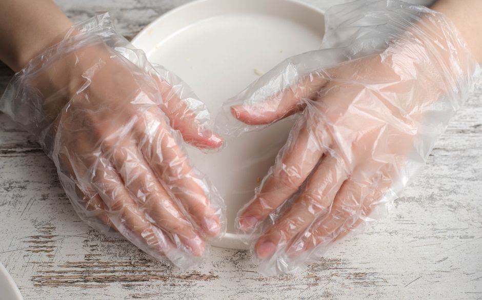 Mãos usando luvas de proteção manipulando alimentos em uma cozinha, focando na higiene e segurança na preparação de alimentos.