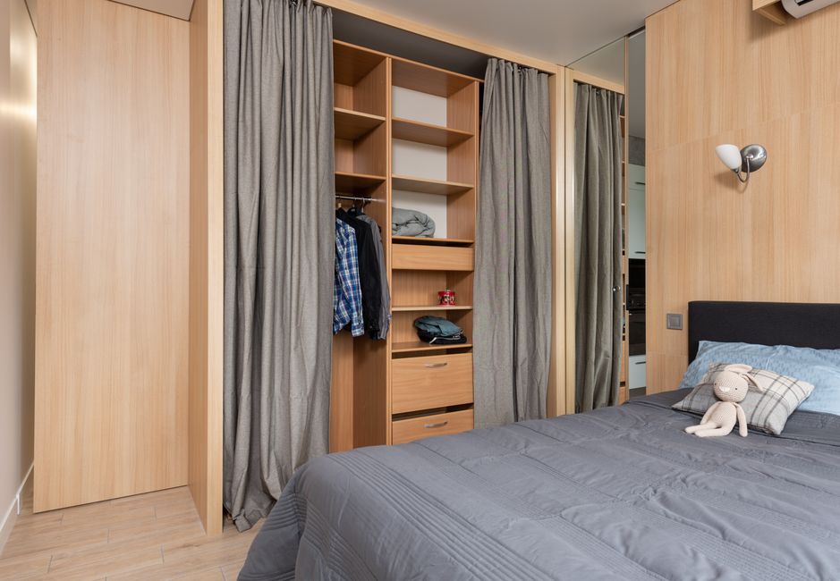 Imagem de um quarto organizado com armário de portas de correr, cama com roupa cinza e um ursinho de pelúcia sobre o lençol, transmitindo um ambiente de conforto e organização.