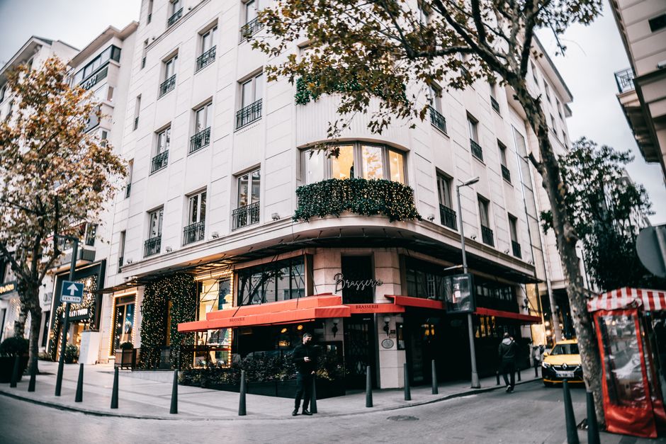 Imagem de um prédio comercial com uma brasserie na esquina, decorado com luzes natalinas, em um ambiente urbano e movimentado.