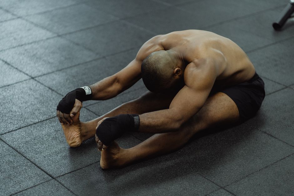 Homem em posição de alongamento ou meditação em um ambiente de academia, focado em bem-estar e flexibilidade.
