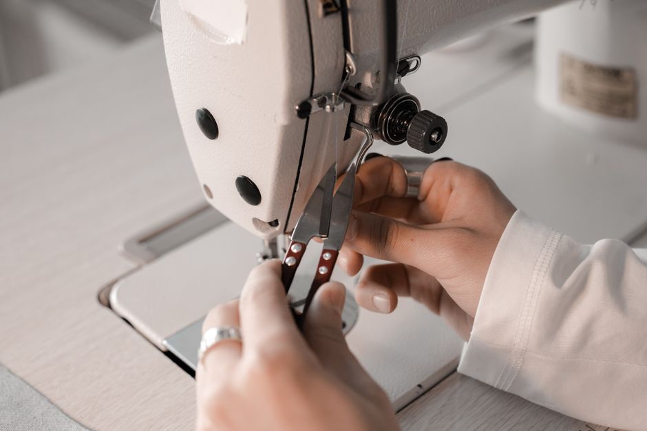 Pessoa operando uma máquina de costura industrial para confecção de roupas ou acessórios.