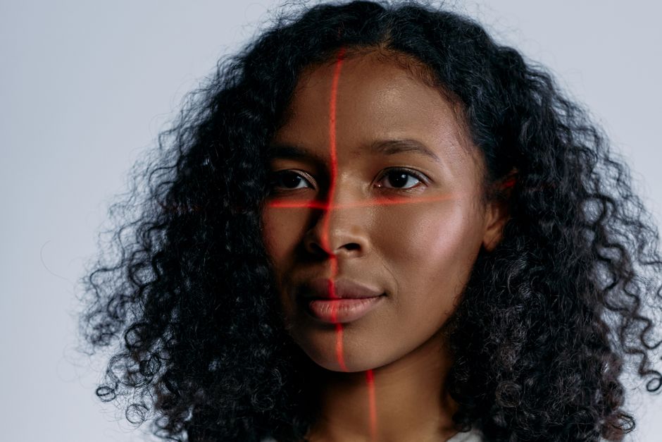 Mulher olhando fixamente para a câmera com uma marca de laser cruzada em seu rosto, simbolizando tecnologia e inovação.