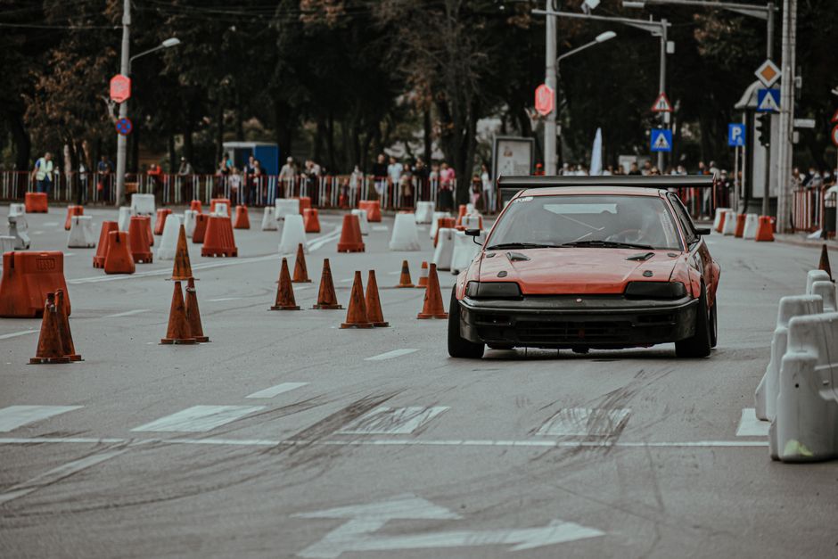 Carro derrapando em uma rua fechada com cones de trânsito, criando uma cena de corrida ou técnica de direção esportiva.