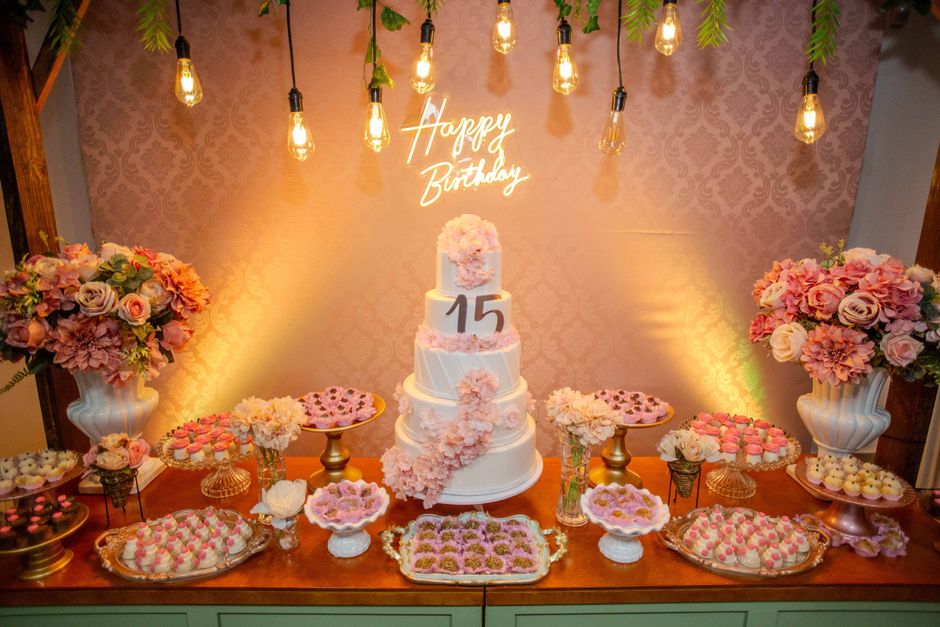 Mesa decorada para festa de 15 anos com bolo, flores e iluminação aconchegante, ideal para celebrações especiais.