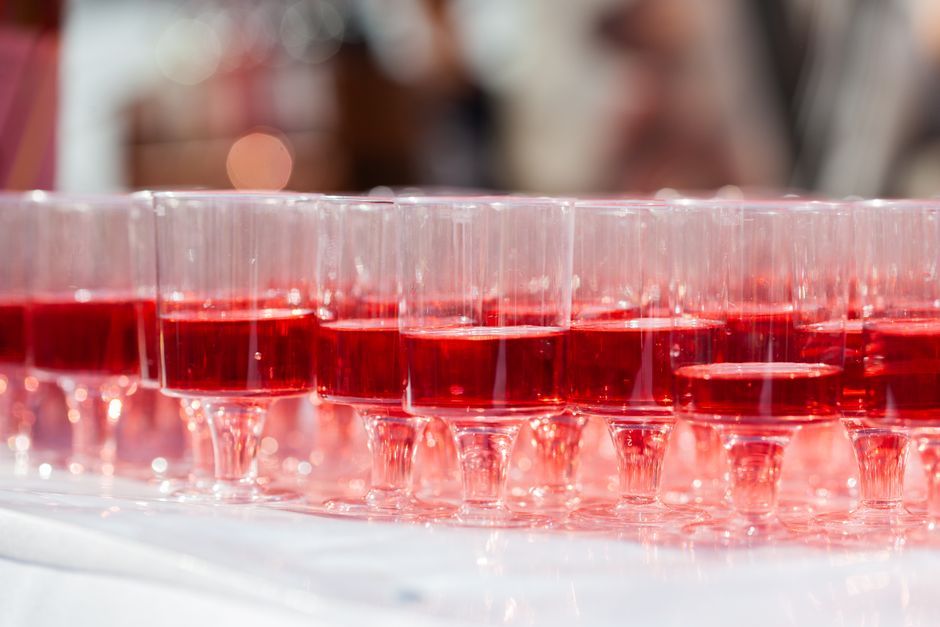Copa de coquetel de cor vermelha preparada para evento social, exibida em fila com fundo desfocado.