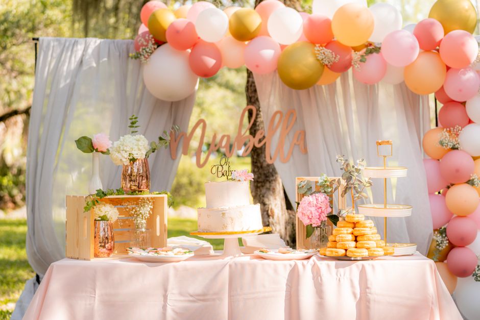 Decoração de festa ao ar livre com balões coloridos, bolo e arranjos de flores, ideal para celebrações infantis ou de chá de bebê.