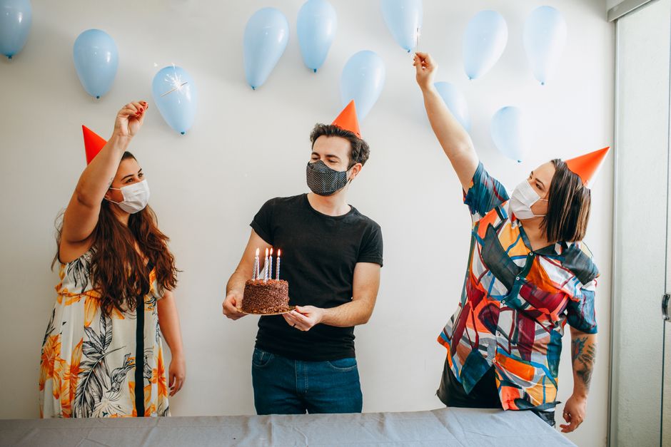 Celebrando aniversário de forma segura e alegre com amigos usando máscara, balões e chapéus na decoração da festa.
