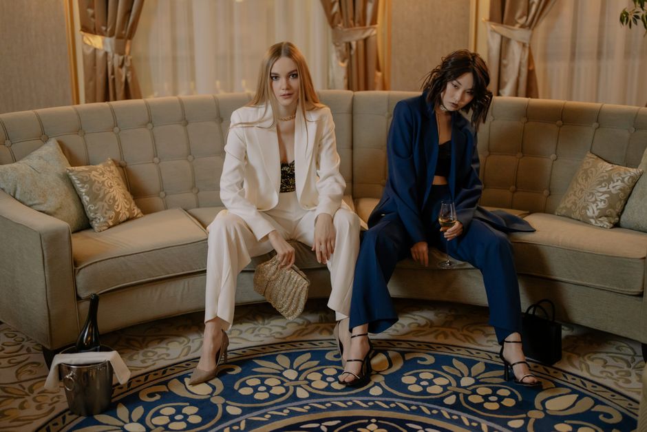 Duas mulheres jovens em um ambiente elegante, sentadas em um sofá, transmitindo uma atmosfera de socialização e estilo em um evento ou reunião.